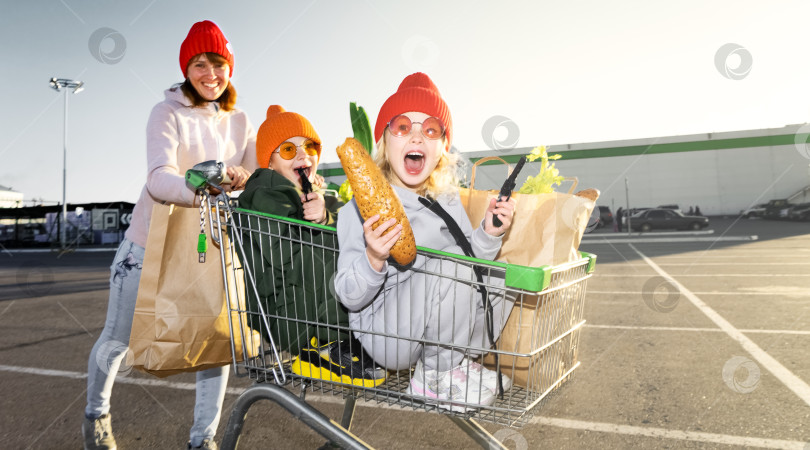 Скачать Мама катает мальчика и девочку в продуктовой тележке детей возле супермаркета фотосток Ozero