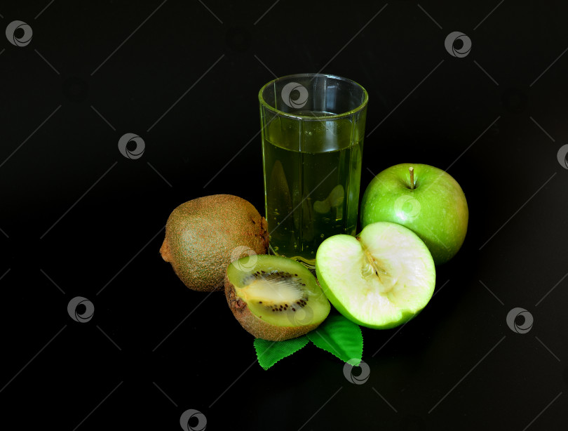 Скачать Стакан фруктового сока на черном фоне, рядом с кусочками спелого киви и зеленым яблоком с листьями. фотосток Ozero