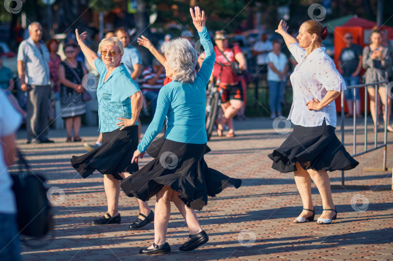 Скачать БЛАГОВЕЩЕНСК, РОССИЯ - 08 июля 2023 года: Группа пожилых женщин в черных юбках танцует на городской площади летним вечером. Концепция увлечений и отдыха пожилых людей фотосток Ozero