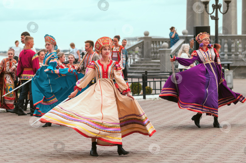 Скачать БЛАГОВЕЩЕНСК, РОССИЯ - 15 июля 2023 года: Девушки в национальных костюмах исполняют танец с мечами на городской набережной во время фольклорного фестиваля. Колонны ротонды на заднем плане фотосток Ozero