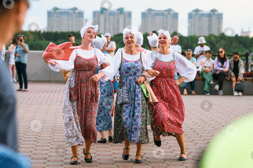 Скачать БЛАГОВЕЩЕНСК, РОССИЯ - 15 июля 2023 года: Женщины в деревенских костюмах танцуют на фольклорном фестивале. Зрители стоят вокруг выступающих на набережной фотосток Ozero