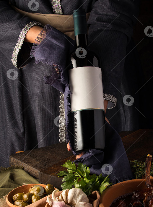 Скачать Вертикальный снимок человека в традиционном костюме, показывающего бутылку вина фотосток Ozero