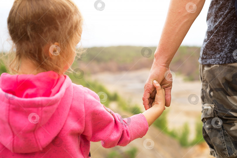 Скачать Дочь в розовой толстовке с капюшоном, держащая папу за руку, стоит на вершине горы с прекрасным панорамным видом. Семейный кемпинг, мероприятия на свежем воздухе. Помощь и поддержка, воспитание детей, защита. фотосток Ozero