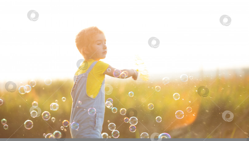 Скачать Девушка в джинсовом комбинезоне пускает мыльные пузыри летом в поле на закате. Международный день защиты детей, счастливый ребенок, мероприятия на свежем воздухе. Летний фон. Здоровый и экологичный образ жизни фотосток Ozero