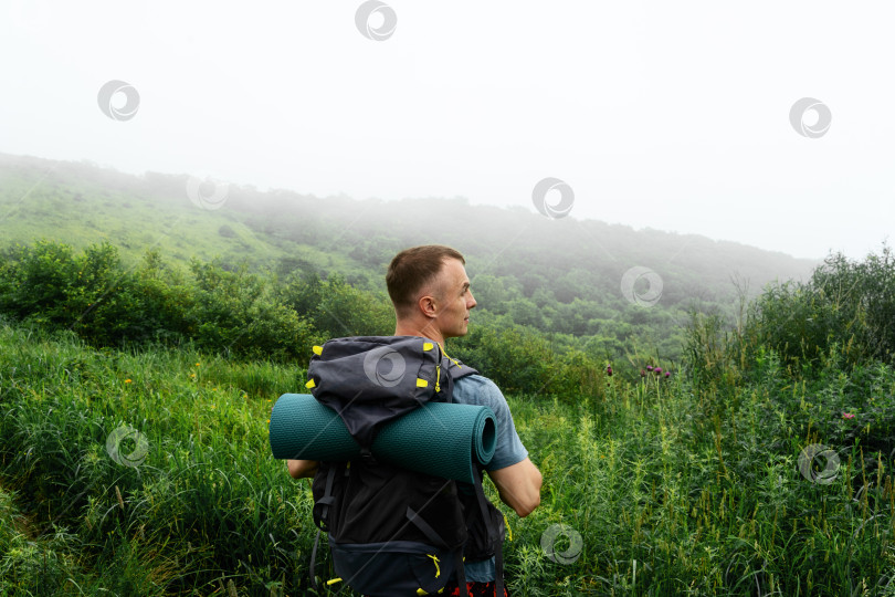 Скачать Турист с большим дорожным рюкзаком поднимается по горной тропе среди высокой травы. фотосток Ozero