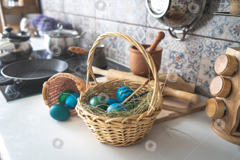 Скачать Праздник Пасхи: Плетеная корзина с цветными крашеными яйцами на кухонном столе. фотосток Ozero
