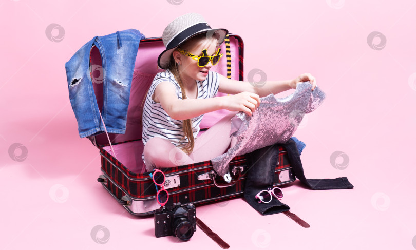 Скачать Путешествие: Девочка-школьница готовится к поездке и собирает одежду в большой чемодан. фотосток Ozero