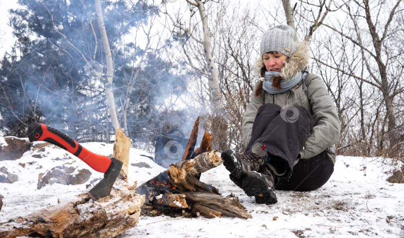 Скачать Пеший туризм: Девушка в серой шапочке на привале греется у костра зимой в горах. фотосток Ozero