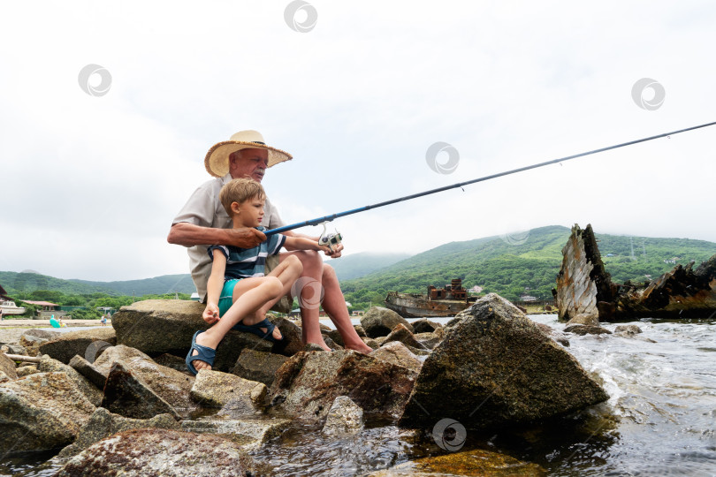 Скачать Дедушка-рыбак в соломенной шляпе и маленький внук мужского пола, наслаждающиеся досугом, пользуются удочкой фотосток Ozero