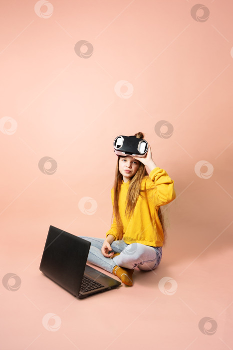 Скачать Девушка-школьница в очках виртуальной реальности с ноутбуком на коленях на розовом фоне. фотосток Ozero