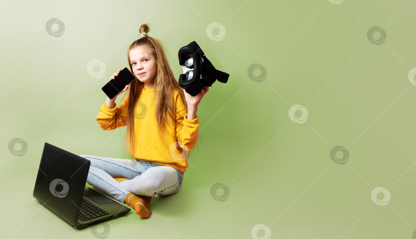 Скачать Счастливая симпатичная девочка позирует с современным цифровым устройством мобильным телефоном vr гарнитурой и портативным ПК фотосток Ozero