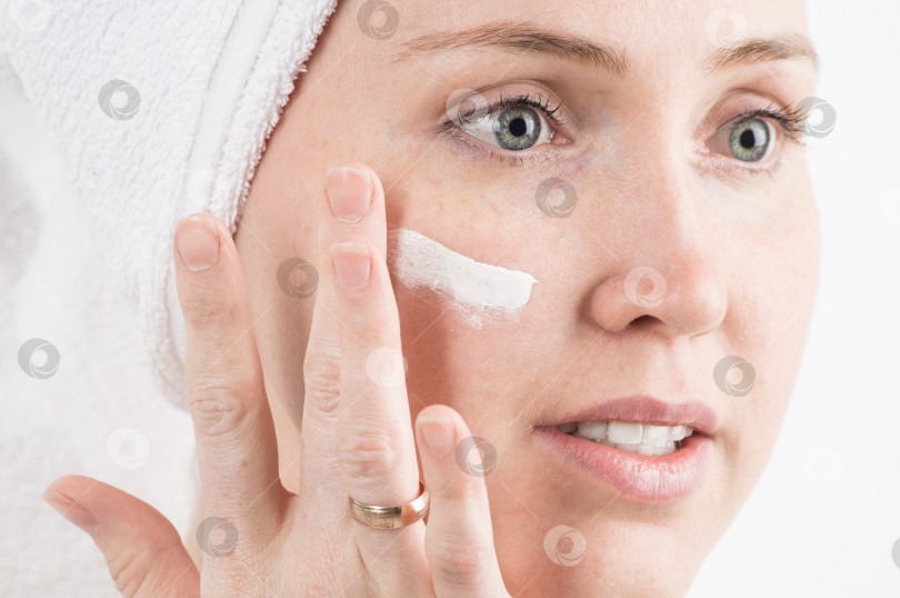 Скачать Косметика: девушка с белым полотенцем на голове наносит на лицо увлажняющий крем. фотосток Ozero