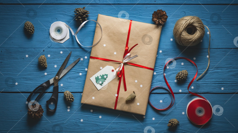 Скачать Подарочная упаковка из бумаги ручной работы и красной ленты на синих деревянных досках с белыми снежинками фотосток Ozero