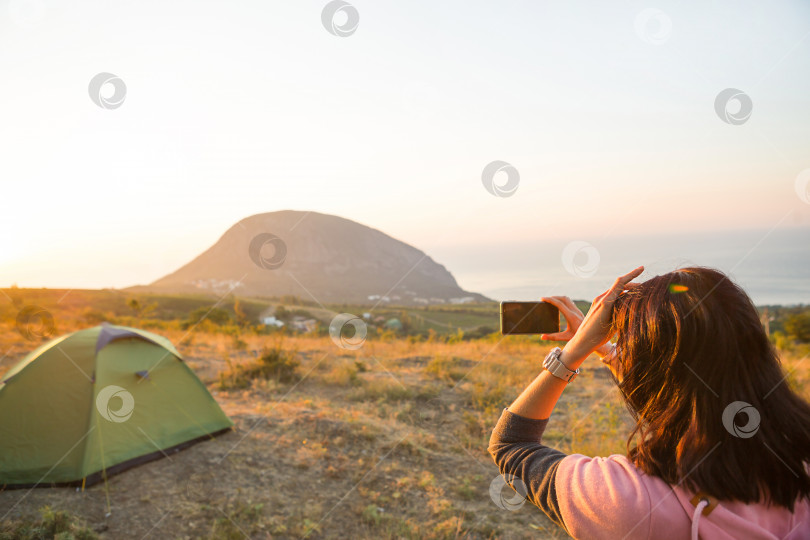 Скачать Женщина фотографирует восход солнца в горах на свой телефон. Селфи в лучах восходящего солнца. Панорамный вид на море и Аю-Даг. Кемпинг, активный отдых, спортивные походы в горы, семейные путешествия. Крым. фотосток Ozero