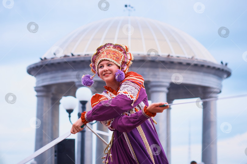 Скачать Девушка в русском национальном костюме и кокошнике танцует с саблями на фоне ротонды. фотосток Ozero