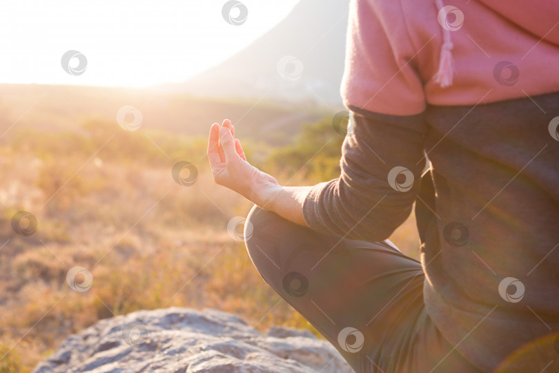 Скачать Женщина сидит на камне в позе лотоса, сомкнув пальцы в знак гармонии, расслабления и медитации. Йога, самопогружение, баланс с природой. Горы, солнечный свет. пространство для копирования фотосток Ozero
