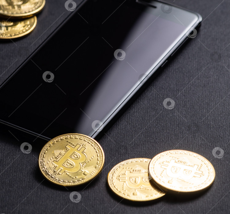 Скачать Заработок на криптовалютах: золотые монеты биткоин и смартфон на темном фоне. Квадратная рамка. фотосток Ozero