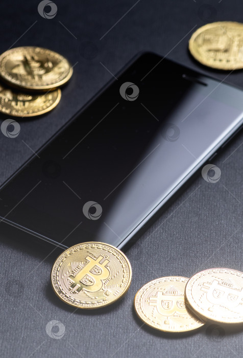 Скачать Заработок на криптовалютах: золотые монеты биткоин и смартфон на темном фоне. Вертикальный снимок. фотосток Ozero