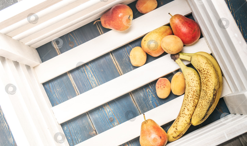 Скачать Здоровая пища: Спелые свежие бананы, груши, абрикосы на дне деревянной коробки. фотосток Ozero