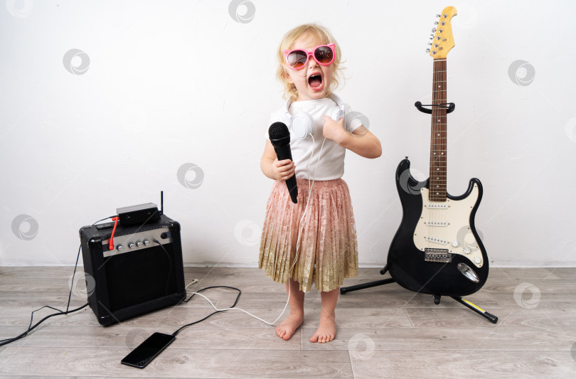 Скачать Домашнее выступление: Молодая девушка сидит на полу и поет в микрофон. Рядом стоит музыкальное оборудование. фотосток Ozero