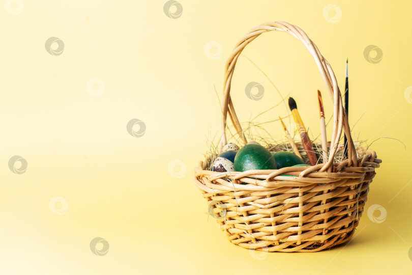 Скачать Пасхальный декор: Простая корзинка с крашеными яйцами и кисточками для росписи на желтом фоне. фотосток Ozero