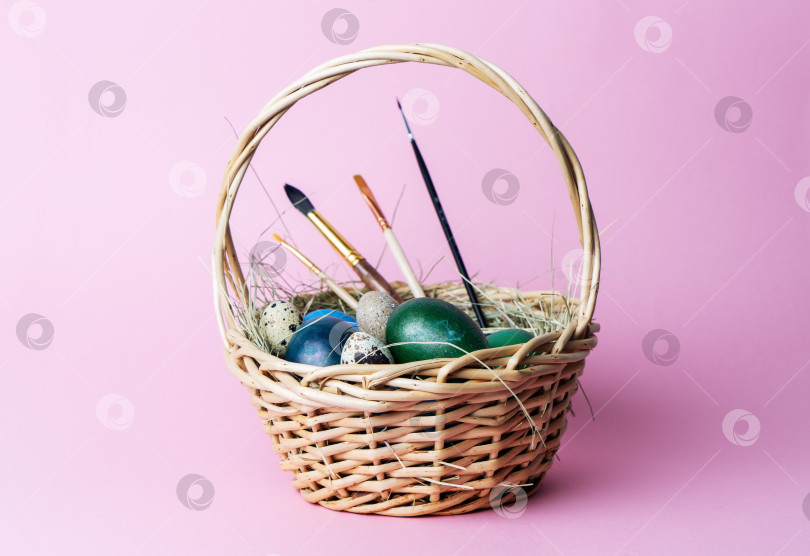 Скачать Пасхальный декор: Простая корзинка с крашеными яйцами и кисточками для росписи на розовом фоне. фотосток Ozero
