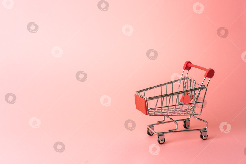 Скачать Красная миниатюрная тележка из супермаркета на розовом фоне. Крупный план. фотосток Ozero