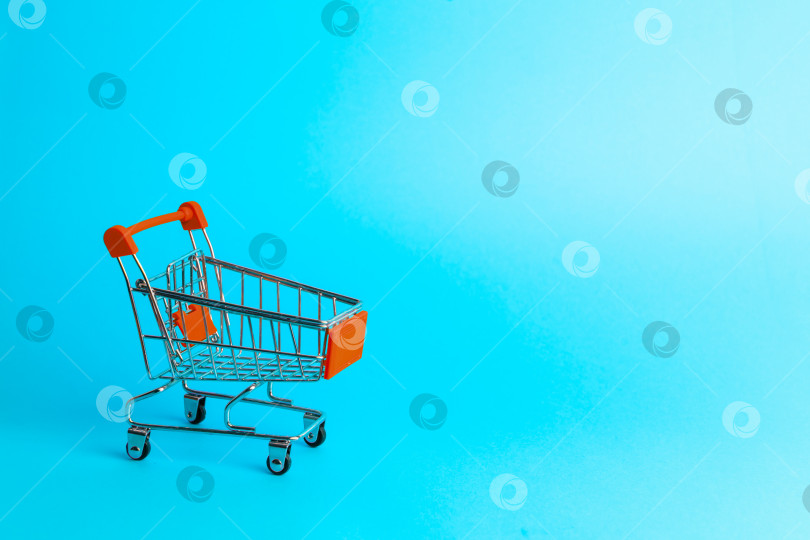 Скачать Покупки для женщин: пустая миниатюрная красная тележка из супермаркета на синем фоне. фотосток Ozero