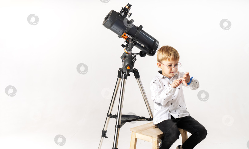 Скачать маленький мальчик, ожидающий астрономического события, сидит возле телескопа и смотрит на свои часы. фотосток Ozero