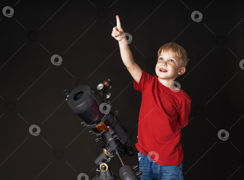 Скачать Маленький мальчик стоит с большим телескопом и указывает пальцем наверх. фотосток Ozero