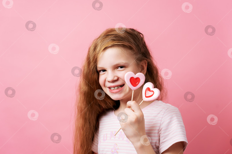 Скачать Девушка держит в руках большие леденцы в форме сердца на розовом фоне. фотосток Ozero