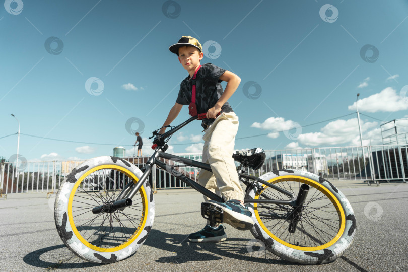 Скачать Мальчик в кепке и футболке катается на велосипеде bmx и учится выполнять трюки возле специальной рампы для трюков. фотосток Ozero