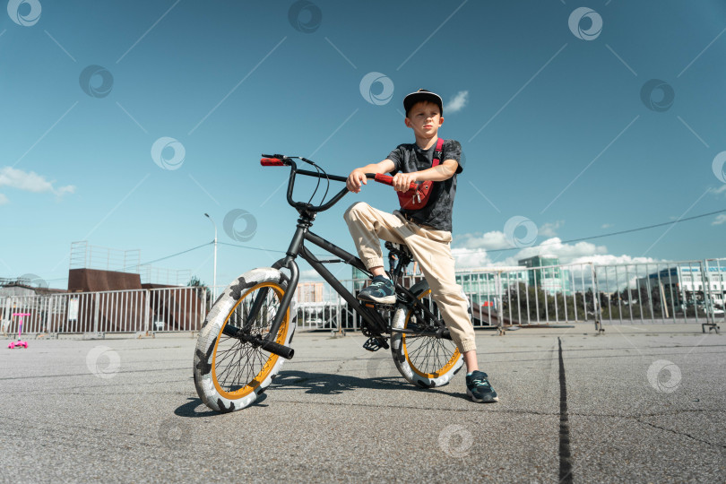 Скачать Мальчик в кепке и футболке катается на велосипеде bmx и учится выполнять трюки возле специальной рампы для трюков. фотосток Ozero