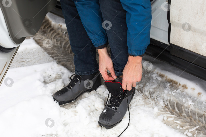 Скачать Мужчина завязывает лыжные ботинки перед тем, как идти по снегу на беговых лыжах. шнурки для обуви, спортивный инвентарь фотосток Ozero
