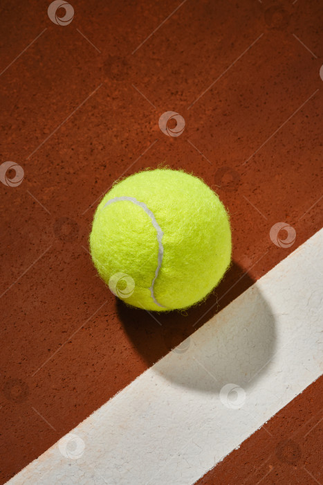 Скачать Теннисный желтый мяч на оранжевой поверхности корта с белой полосой. фотосток Ozero