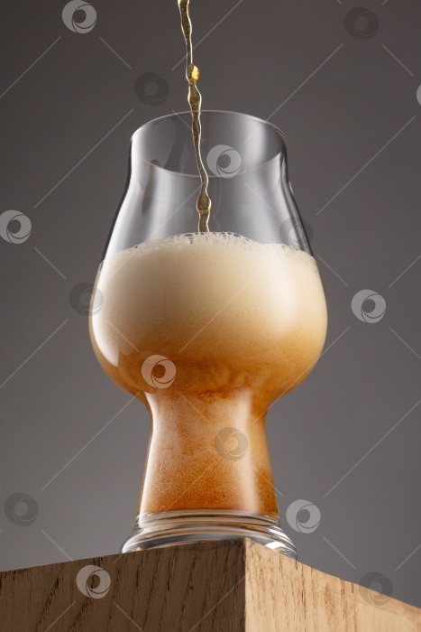 Скачать Бокал свежего и холодного золотистого пива на сером фоне и деревянном подиуме. фотосток Ozero