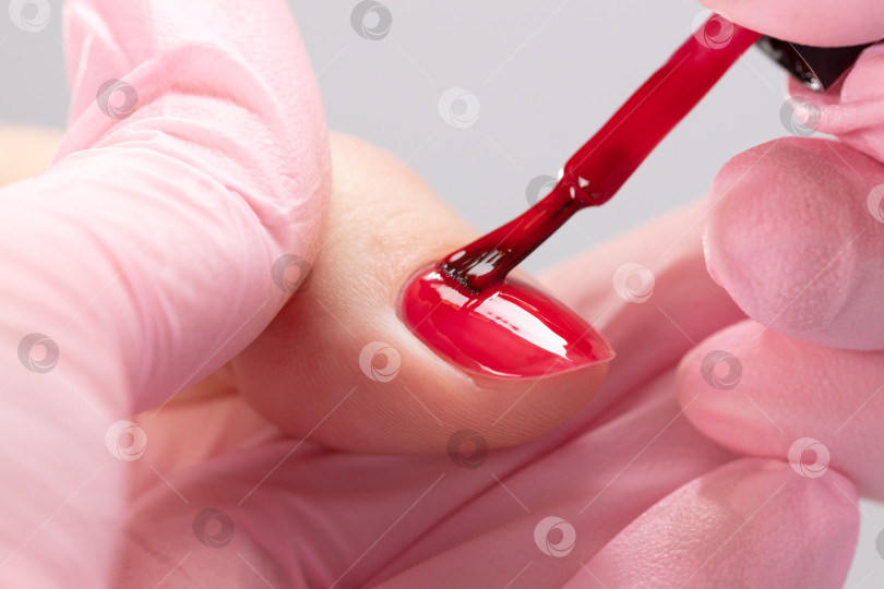 Скачать Косметолог наносит красный лак на женские ногти в маникюрном салоне. фотосток Ozero