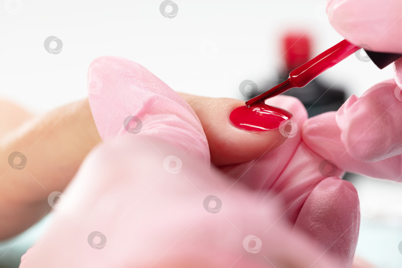 Скачать Косметолог наносит красный лак на женские ногти в маникюрном салоне. Процедура маникюра в маникюрном салоне. фотосток Ozero