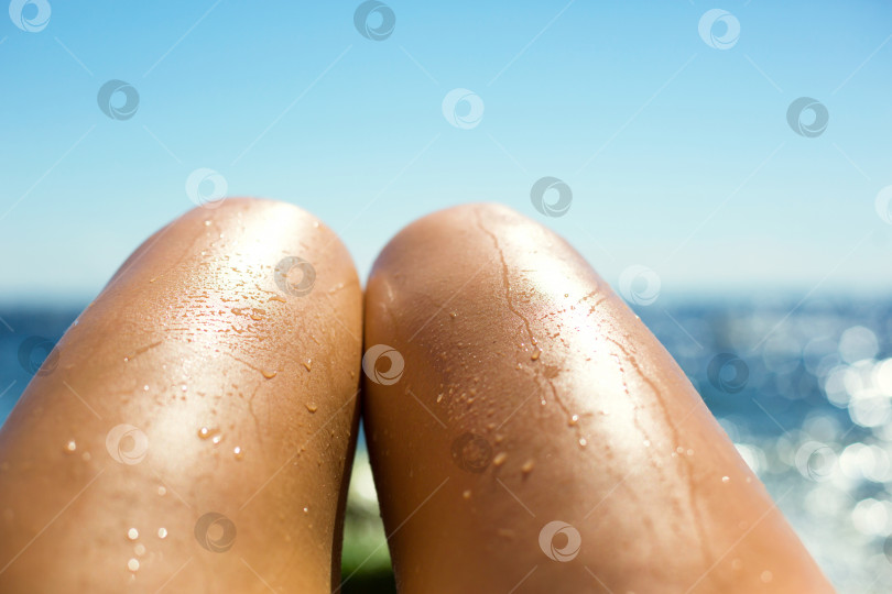 Скачать Гладкие загорелые женские ножки в брызгах воды на пляже на фоне моря. Средства для загара, защита от солнечных ожогов, уход за кожей, депиляция, пляжный отдых. Пространство для копирования фотосток Ozero