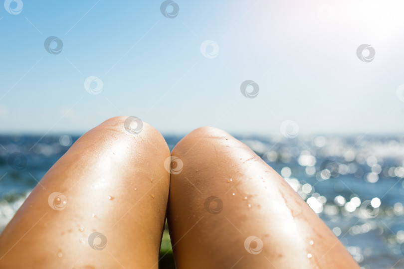 Скачать Гладкие загорелые женские ноги в брызгах воды на пляже на фоне моря. Средства для загара, защита от солнечных ожогов, уход за кожей, депиляция, пляжный отдых. Пространство для копирования фотосток Ozero