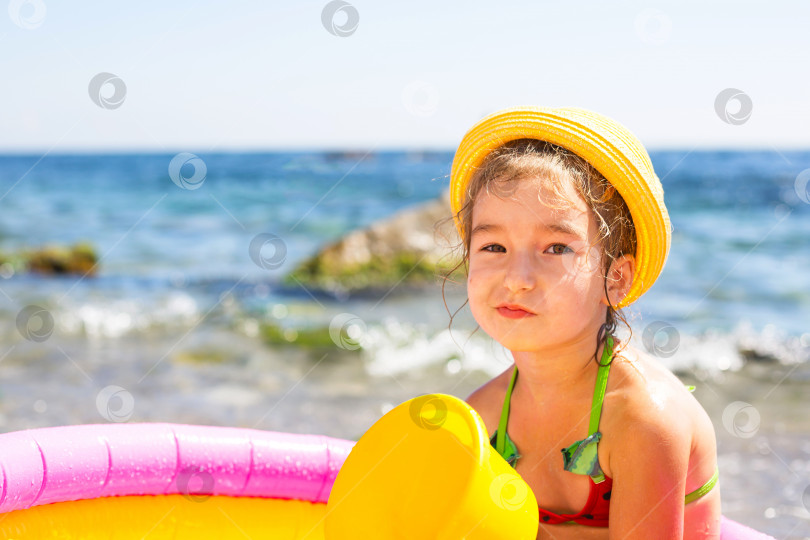 Скачать Девушка в желтой соломенной шляпе сидит в надувном бассейне на берегу моря с серьезным и недовольным видом. Несмываемые средства для защиты детской кожи от солнца, солнечных ожогов. курорт на берегу моря. фотосток Ozero