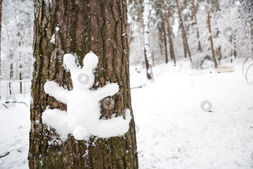 Скачать Снеговик в форме зайца прилеплен к стволу дерева. Веселые зимние развлечения, дети и семья играют в снегу. Пространство для копирования фотосток Ozero