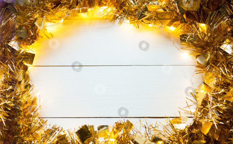 Скачать Праздничная рамка из золотой гирлянды с огнями и мишурой на белом деревянном фоне, copyspace. Новый год, Рождество, осень и зима согревают атмосферу. фотосток Ozero
