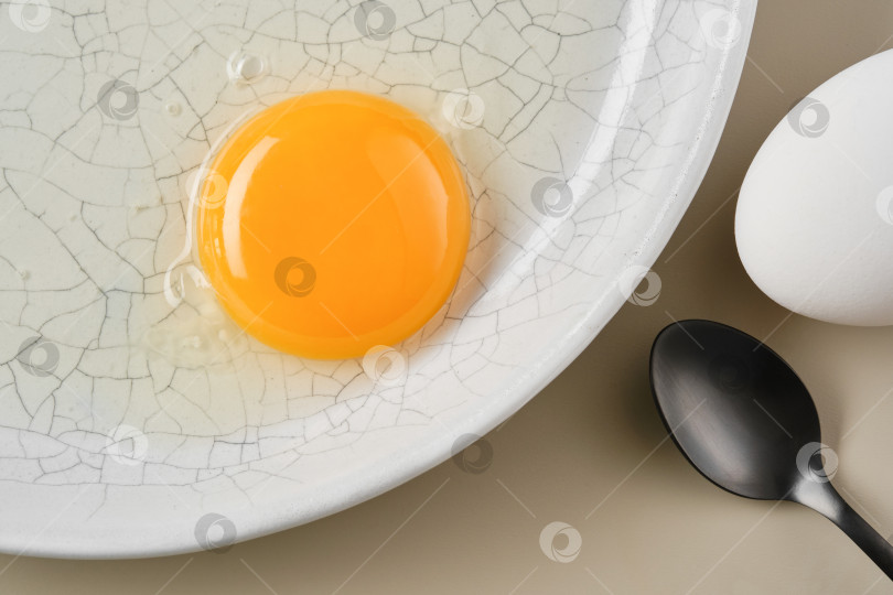 Скачать Разбитое яйцо с желтым желтком в белой тарелке и черной ложке. фотосток Ozero