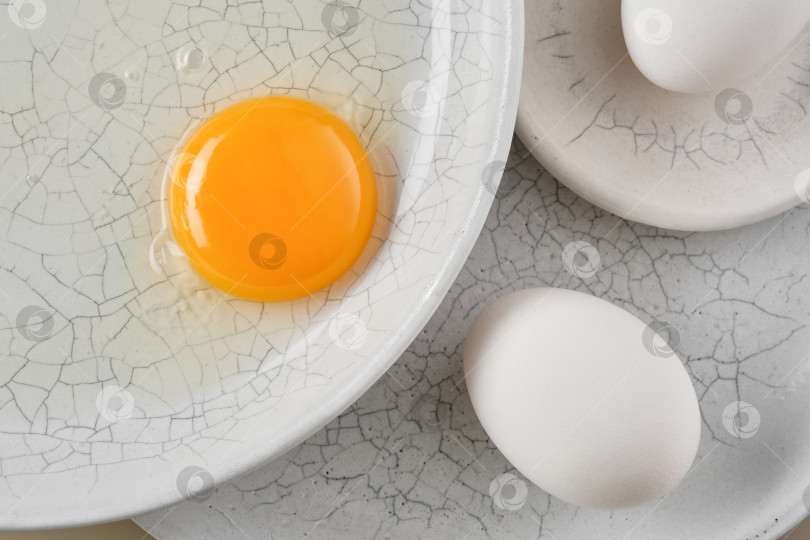 Скачать Разбейте яйцо с желтком в белую тарелку и проделайте отверстия в белых яйцах на тарелке. фотосток Ozero