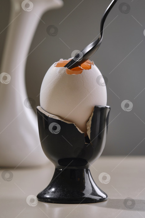 Скачать Разбейте белое яйцо с желтком в разбитую черную керамическую чашку для яиц с помощью черной чайной ложки. фотосток Ozero