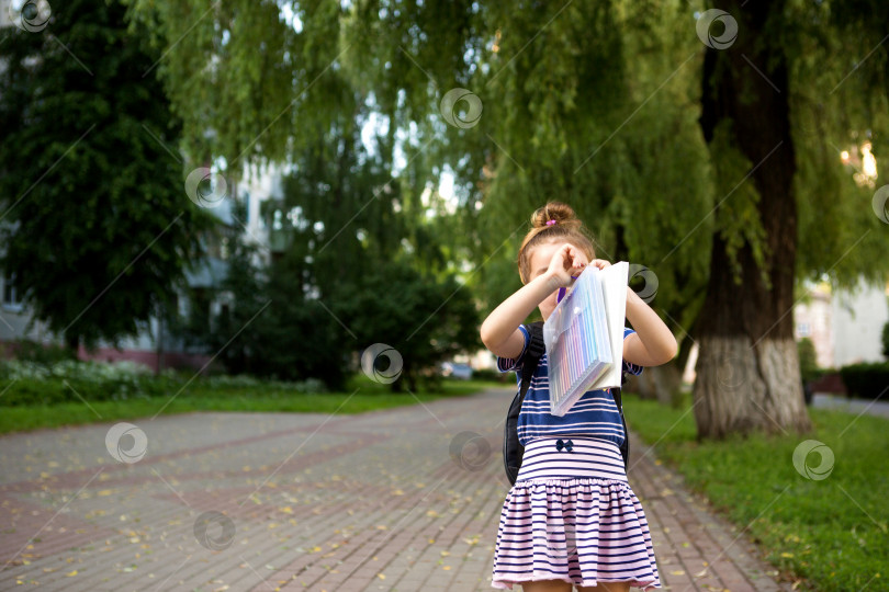 Скачать Маленькая девочка кавказской внешности в школьной форме с рюкзаком, книгой и набором фломастеров. обратно в школу. Начальная школа, развивающие занятия для дошкольников. Пространство для текста фотосток Ozero