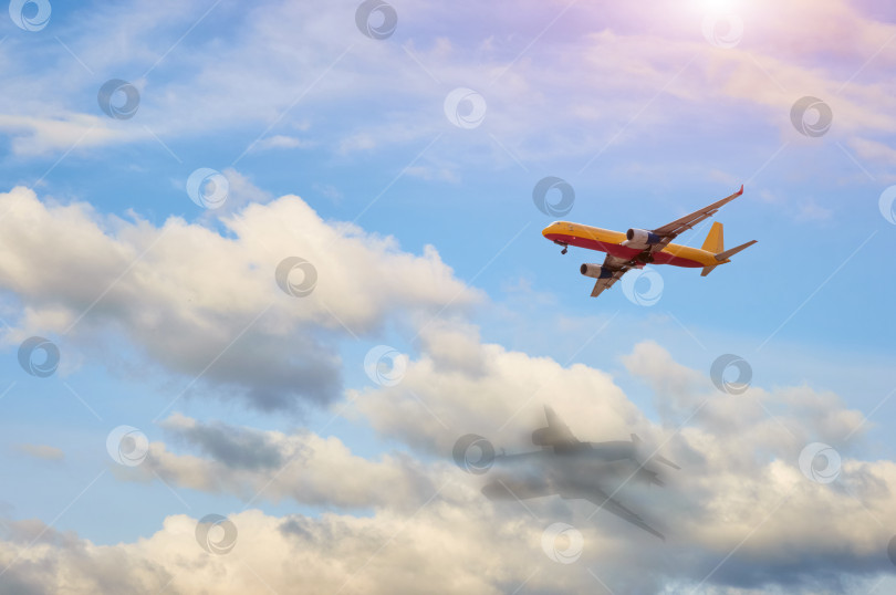 Скачать Грузовой реактивный самолет летит среди белых облаков в голубом небе в солнечную погоду. Тень самолета на облаках фотосток Ozero