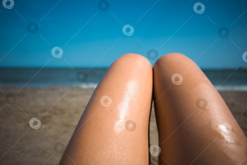 Скачать Женщина на пляже мажет ноги солнцезащитным лосьоном из оранжевого тюбика. Уход за кожей, защита от ультрафиолета, солнцезащитный крем. Пляжный отдых фотосток Ozero