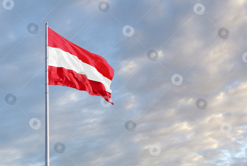 Скачать Развевающийся австрийский флаг на фоне голубого неба с облаками и пустым пространством для текста. фотосток Ozero